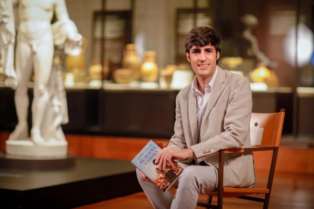 Alfonso Goizueta, sentado, con su libro en la mano, en la sala de un museo.