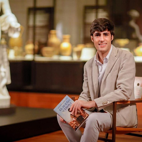 Alfonso Goizueta, sentado, con su libro en la mano, en la sala de un museo.