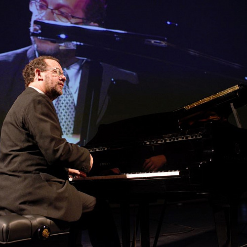 Sergio Feferovich frente a su piano, de fondo se ve a él en una pantalla