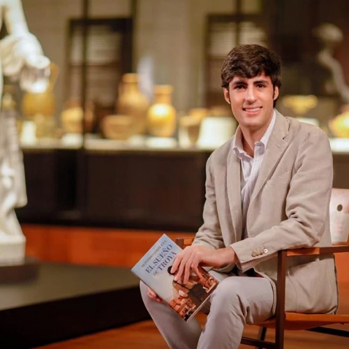 Alfonso Goizueta, sentado, con su libro en la mano, en la sala de un museo.